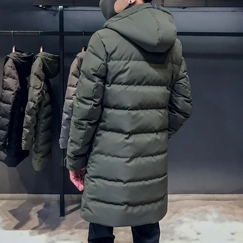 Person wearing olive green puffer jacket with hood in a modern clothing store with jackets on rack