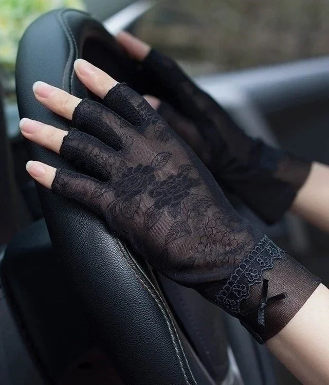 Black floral lace fingerless gloves with bow detail worn on hands holding a car steering wheel