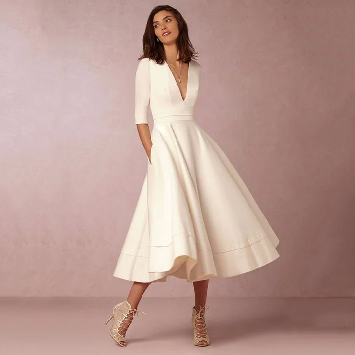 Woman wearing elegant white midi dress with 3/4 sleeves and V-neck, paired with lace-up high heel sandals