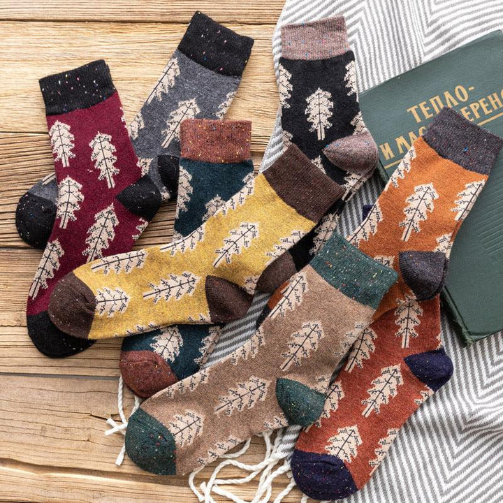Colorful wool socks with leaf patterns arranged on wooden surface and striped fabric, cozy autumn style
