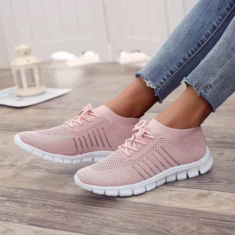 Light pink knit sneakers with white sole worn with frayed hem blue jeans on wood floor