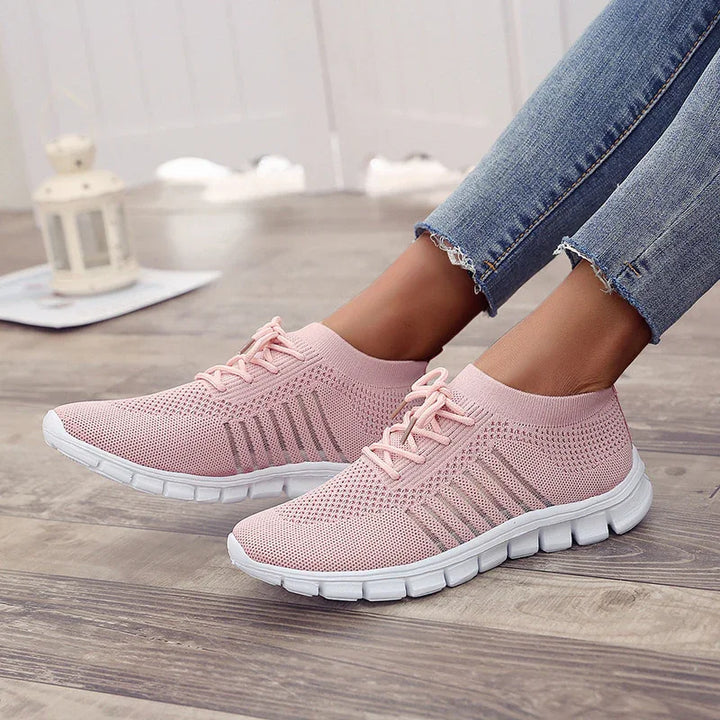 Light pink knit sneakers with white sole worn with frayed hem blue jeans on wood floor