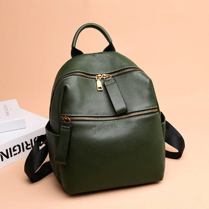 Dark green leather backpack with gold zippers and black adjustable straps on peach background