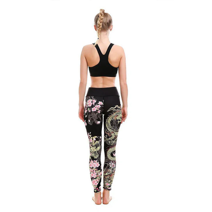 Woman wearing black sports bra and black leggings with colorful dragon and floral print, standing barefoot