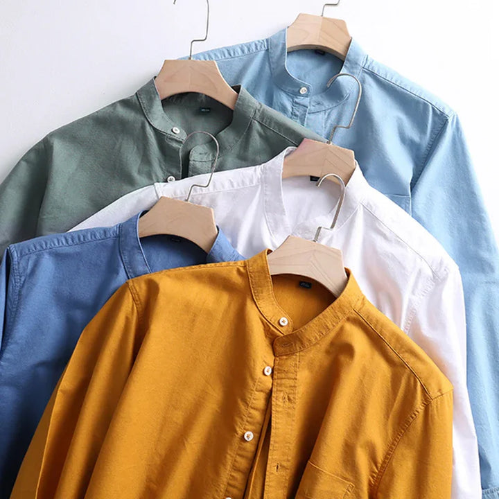 Five mandarin collar shirts in mustard, blue, white, green, and light blue hanging on wooden hangers