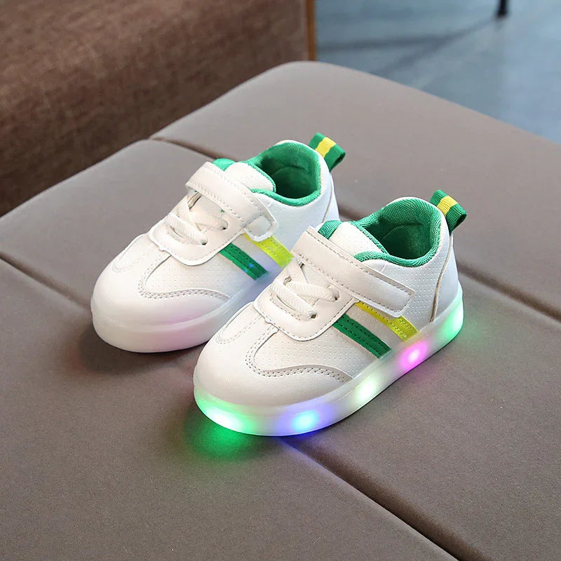 White toddler sneakers with green and yellow accents and colorful LED light-up soles on brown surface