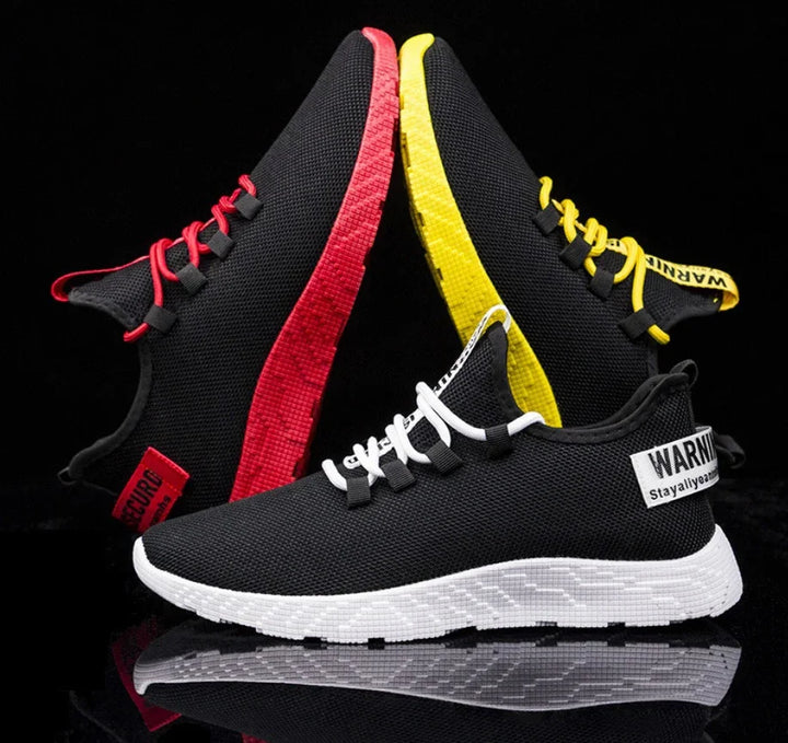 Black mesh sneakers with red, yellow, and white soles and laces on black background
