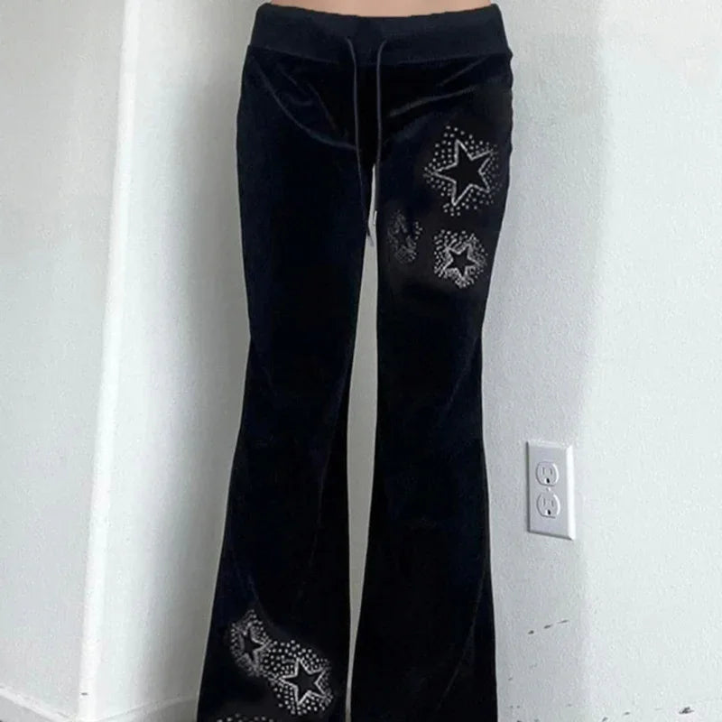 Black velvet flare pants with silver studded star designs on right leg against white wall