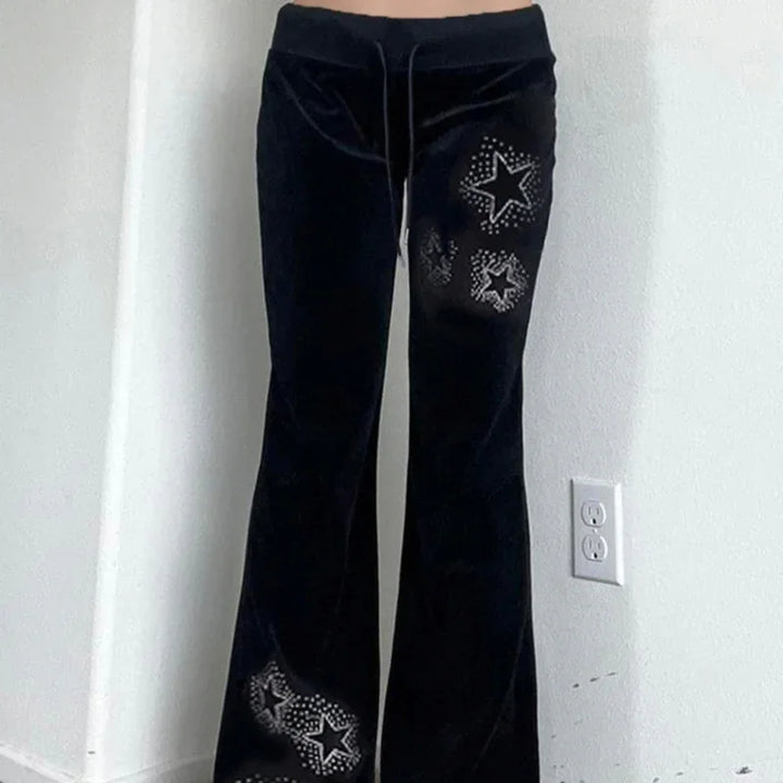Black velvet flare pants with silver studded star designs on right leg against white wall