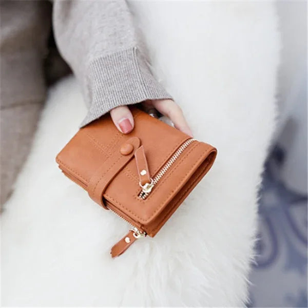 Close-up of hand holding compact brown leather wallet with zipper and snap button on white fuzzy surface