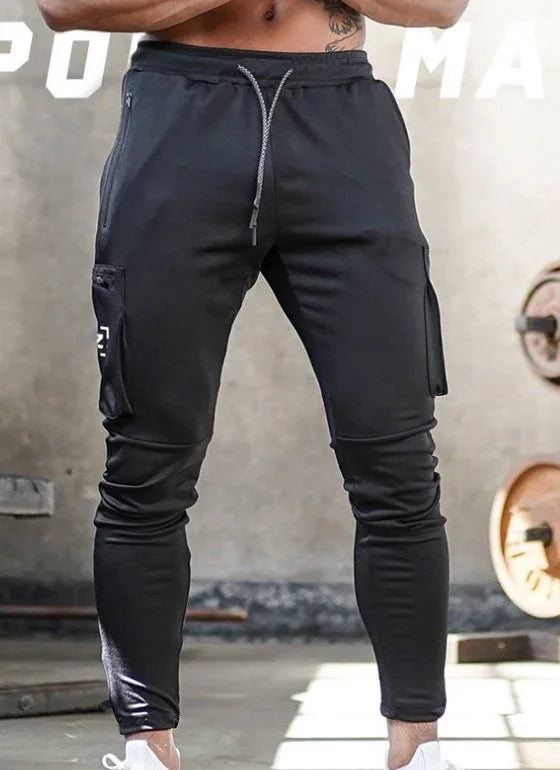 Man wearing black slim-fit cargo jogger pants with drawstring waist and side zipper pockets in gym setting