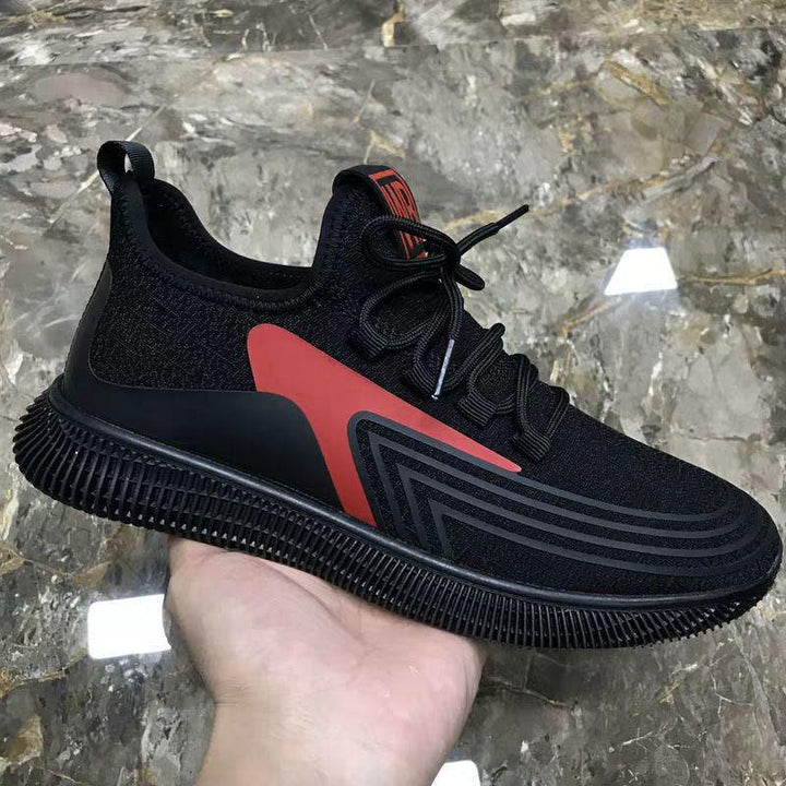 Hand holding a black and red athletic sneaker with textured sole on marble surface