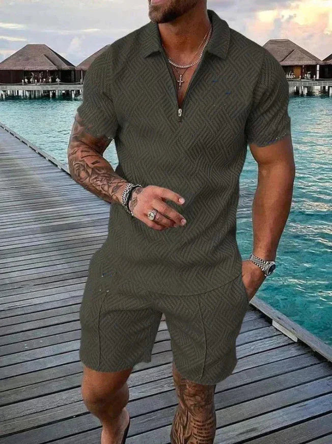 Muscular man wearing dark patterned short-sleeve polo shirt and matching shorts on wooden pier by water villas