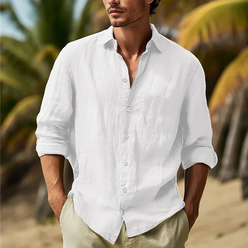 Man wearing white linen shirt with rolled sleeves standing on tropical beach with palm trees