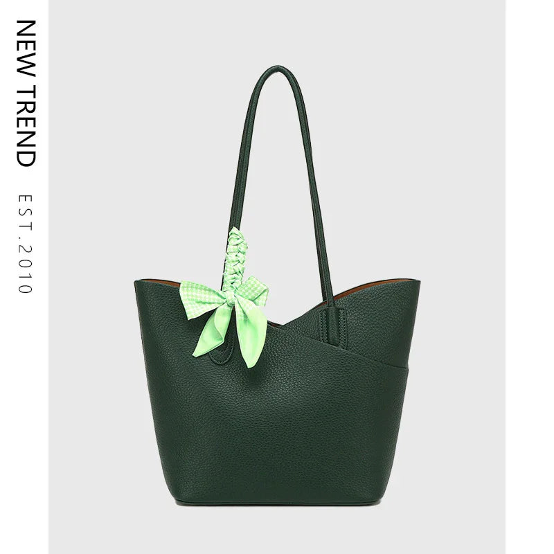 Dark green leather tote bag with long straps and a light green bow accessory on plain background