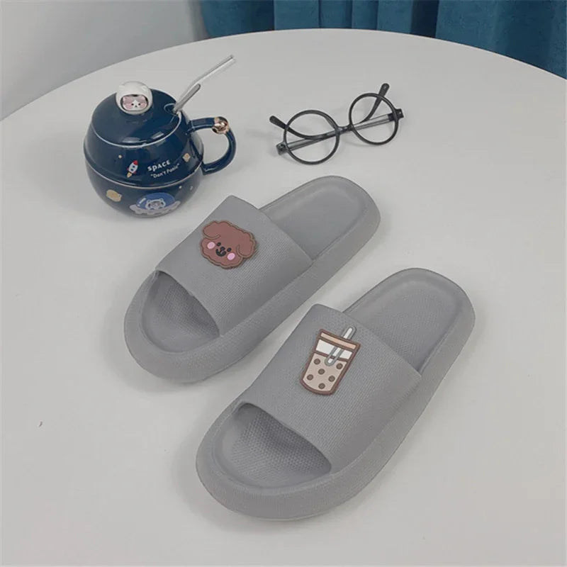Gray slide slippers with cute dog and bubble tea patches on a white table with black round glasses and a navy space-themed teapot