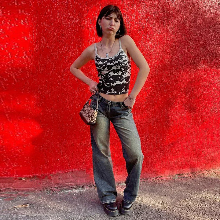Young woman in black and white eye-print tank top and wide-leg jeans posing against vibrant red wall