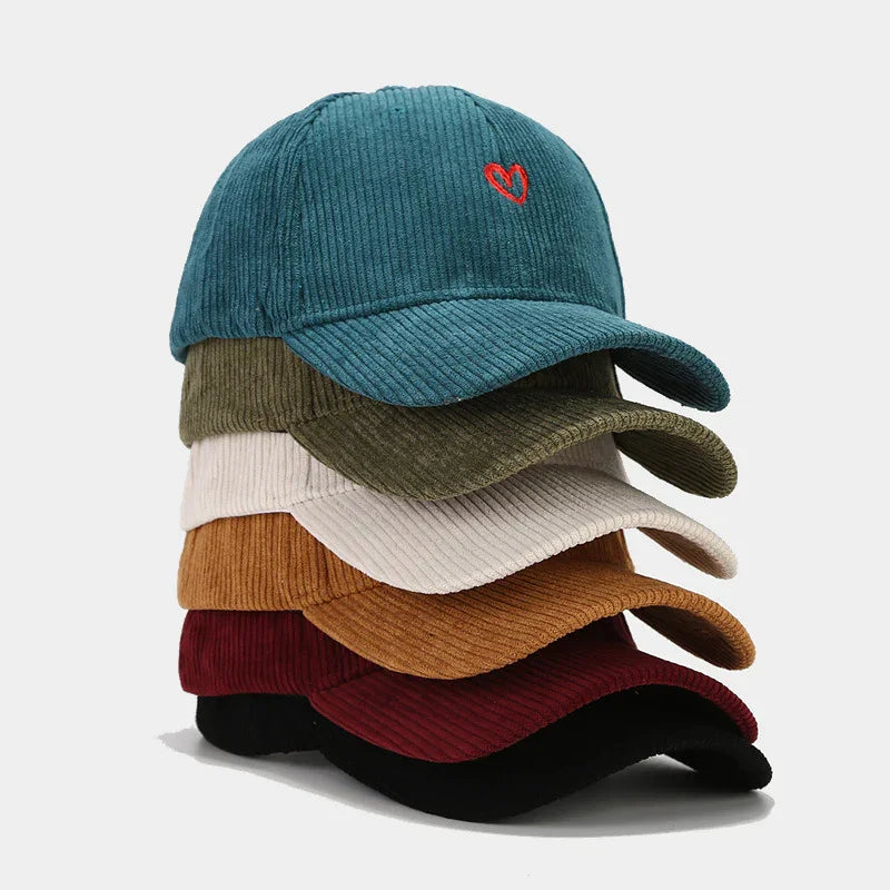 Stack of six corduroy baseball caps in teal with red heart, olive, beige, brown, maroon, and black colors
