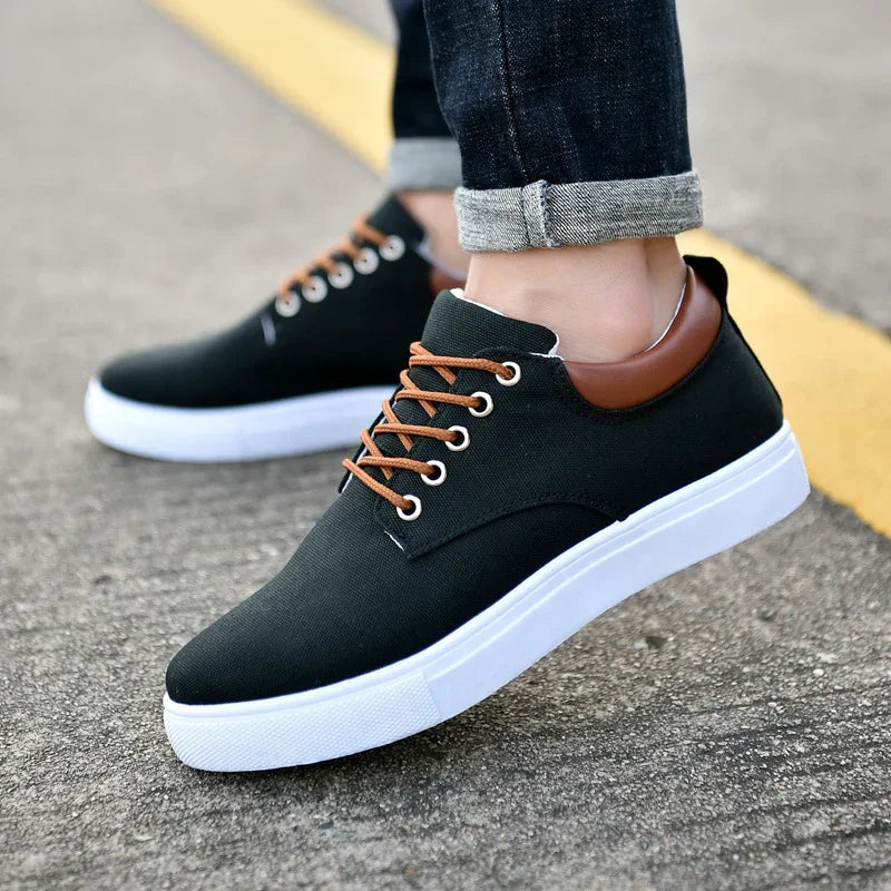 Casual black sneakers with brown laces and collar, white sole, worn with rolled-up dark jeans on pavement