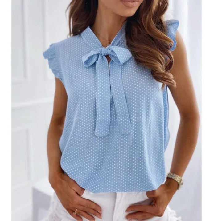 Woman wearing light blue sleeveless polka dot blouse with bow tie neckline and ruffle sleeves