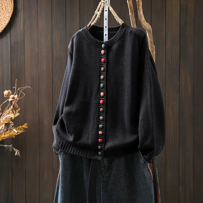 Black knit cardigan with multicolored buttons hanging on rustic rope hanger against wooden backdrop