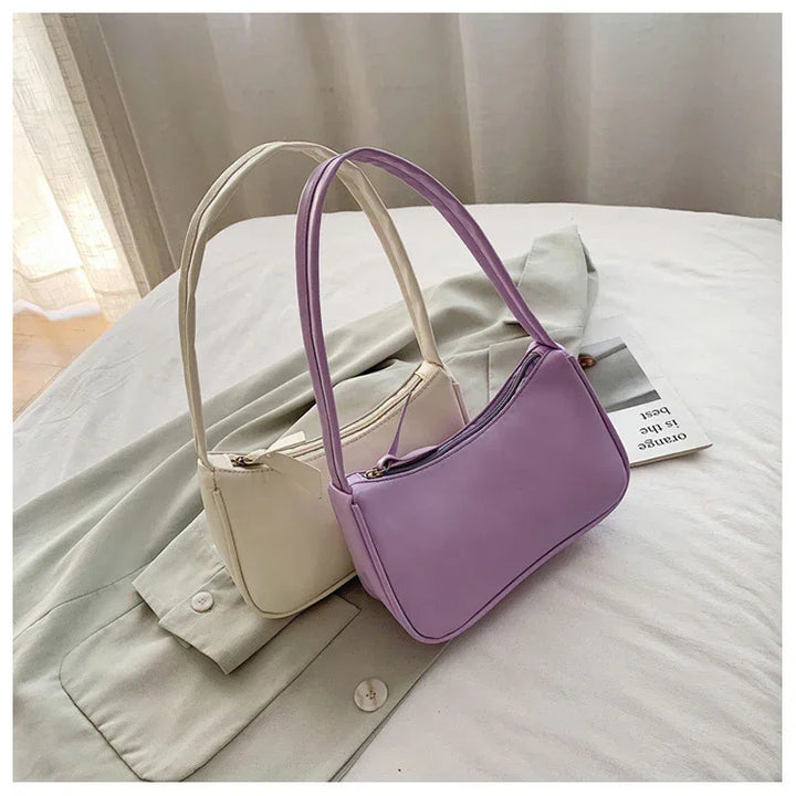 Two minimalist shoulder bags in cream and lavender colors placed on beige jacket on white surface