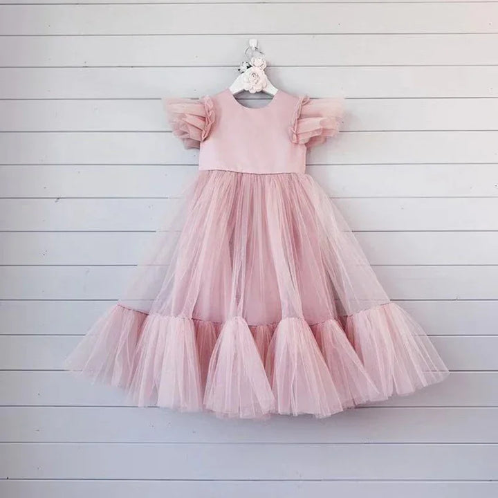 Elegant light pink toddler tulle dress with ruffled sleeves hanging on white wall