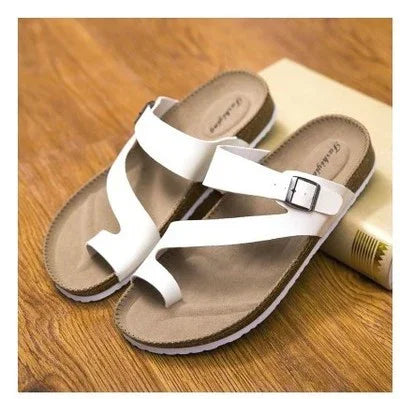 White leather toe-loop sandals with adjustable buckle on wooden floor background