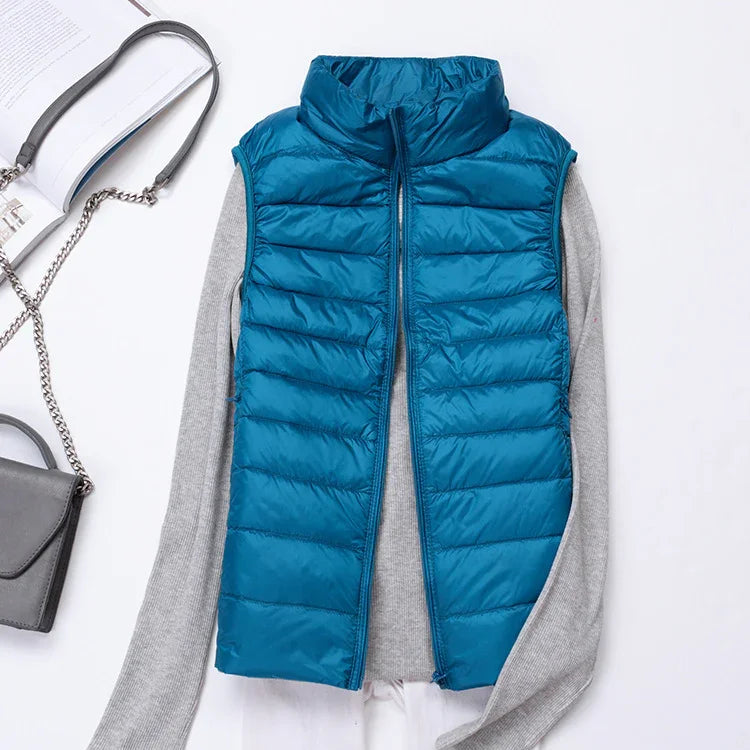 Blue puffer vest over gray long sleeve sweater with gray purse and open book on white surface