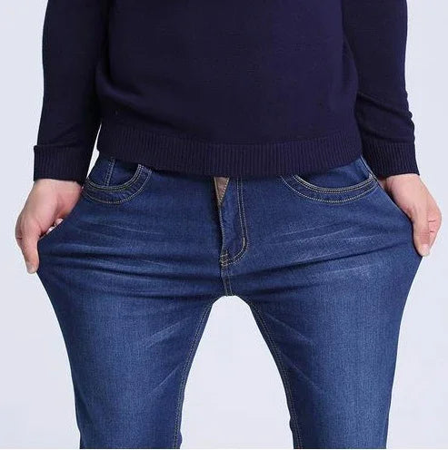 Person wearing dark blue skinny jeans and navy sweater, pulling jeans outward to show stretch