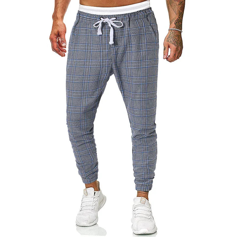Men's grey plaid jogger pants with white drawstring and elastic cuffs, paired with white sneakers