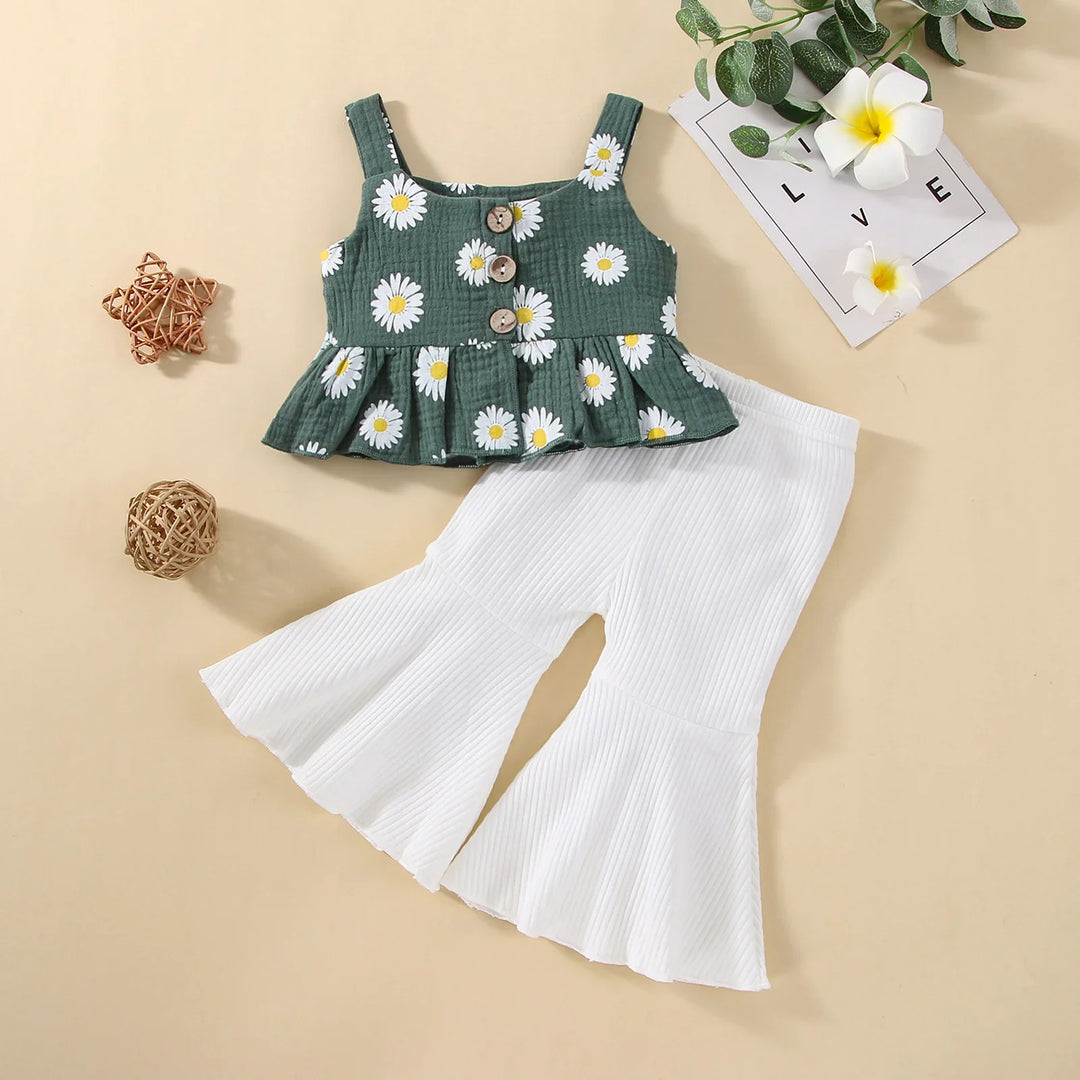 Green baby top with white daisy print and wooden buttons paired with white ribbed flare pants on beige background