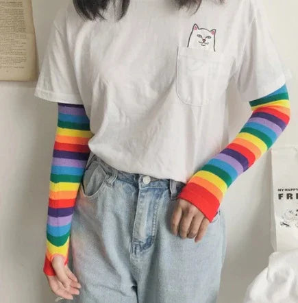 Person wearing white t-shirt with cat pocket design and rainbow-striped long sleeves under light blue jeans