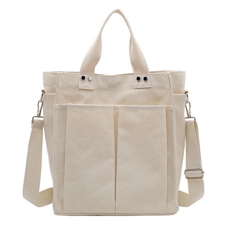 Beige canvas tote bag with dual front pockets, two handles, and adjustable shoulder strap