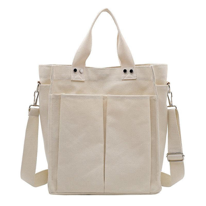 Beige canvas tote bag with dual front pockets, two handles, and adjustable shoulder strap