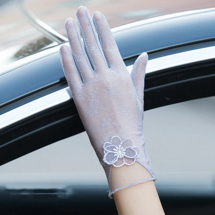 Elegant light gray lace glove with floral embroidery worn on hand above car window