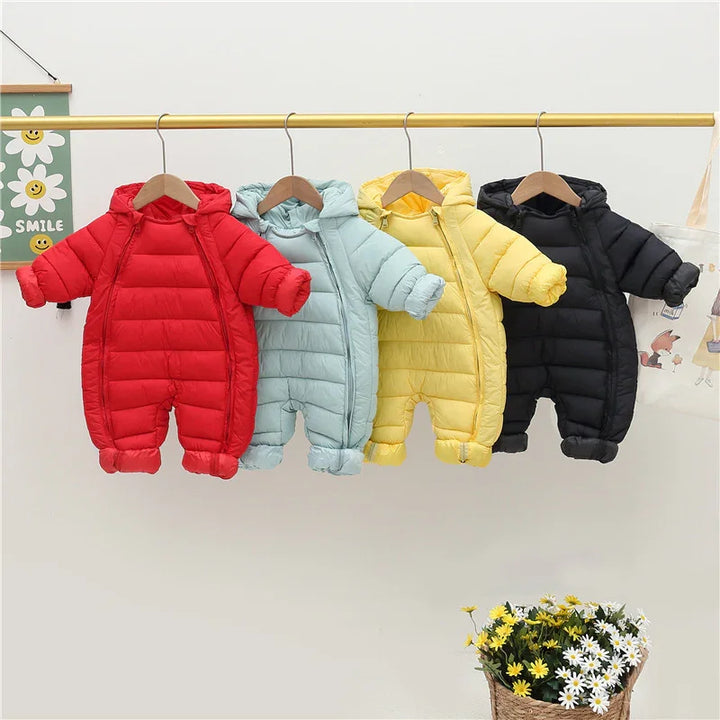 Four colorful baby padded winter jumpsuits with hoods in red, light blue, yellow, and black hanging on a wooden rack