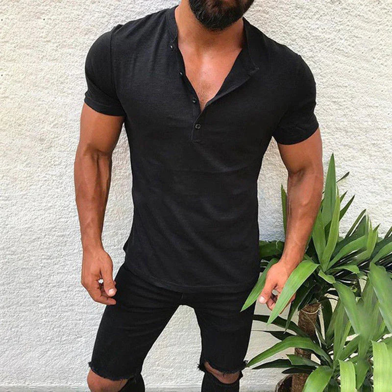 Muscular man wearing black short-sleeve buttoned shirt and ripped black shorts standing by green plants