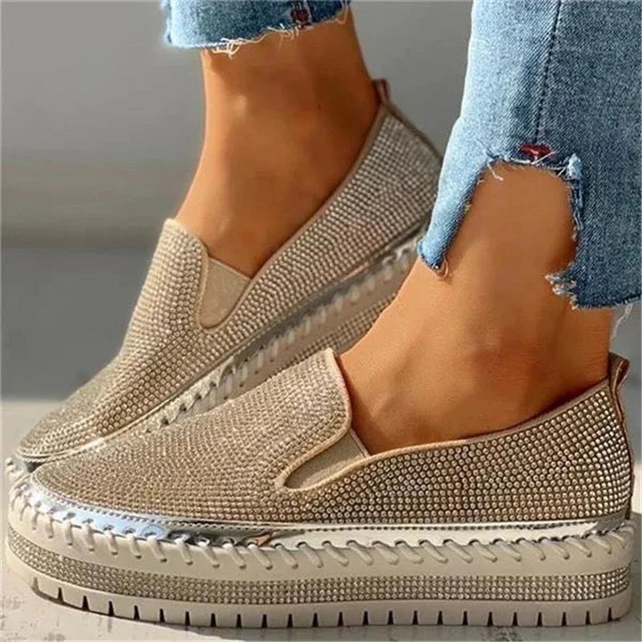 Beige slip-on platform sneakers with rhinestone embellishments and silver accents worn with frayed hem jeans