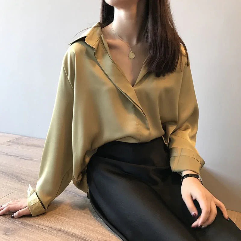 Woman wearing loose mustard yellow blouse and black skirt sitting on wooden floor, minimal jewelry