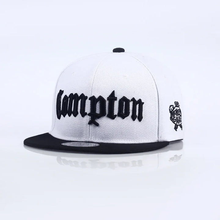 White snapback hat with black brim and bold black 'Compton' embroidery on front