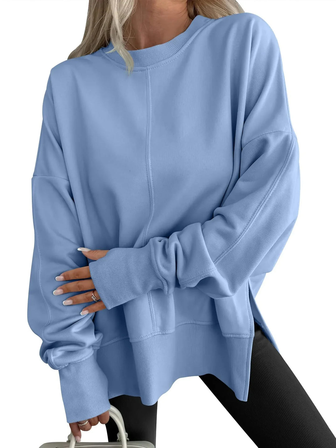 woman wearing oversized light blue sweatshirt with ribbed cuffs holding white handbag