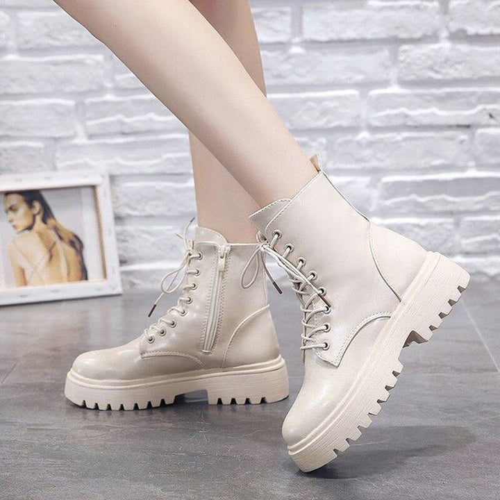 Close-up of beige lace-up combat boots with chunky soles worn on grey floor against white brick wall