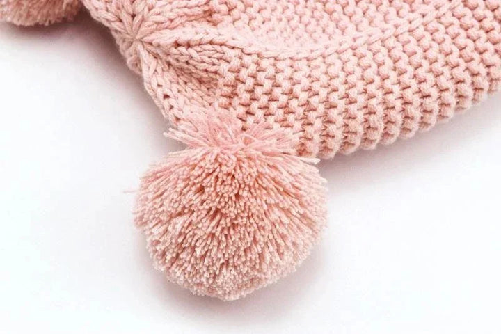 Close-up of soft pink knitted fabric with a large pompom detail on white background