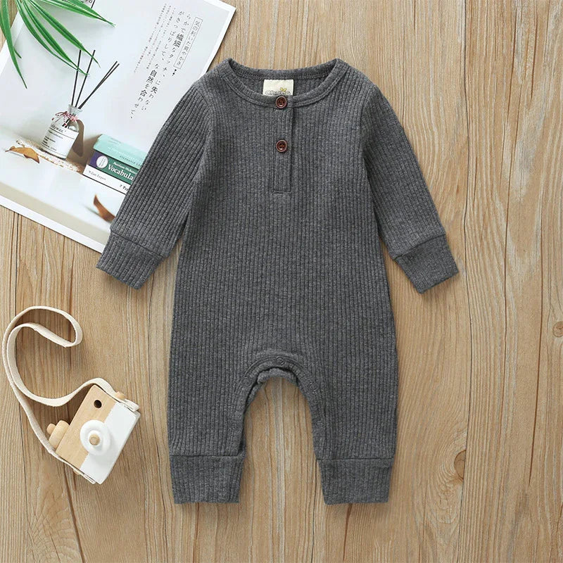 Gray ribbed long-sleeve baby romper with two buttons, wooden toy camera, and books on wooden floor