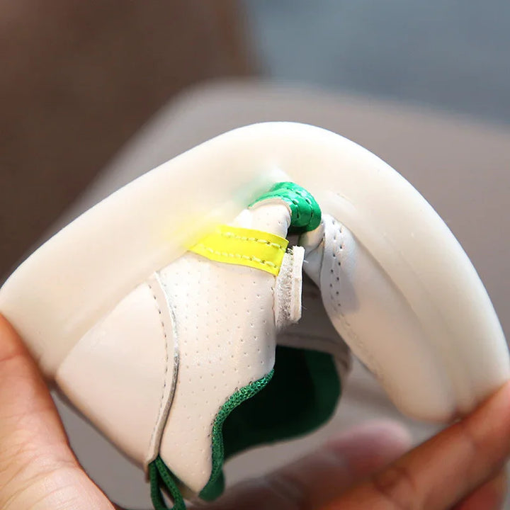 Close-up of a flexible white sneaker with green and yellow accents being folded by hand
