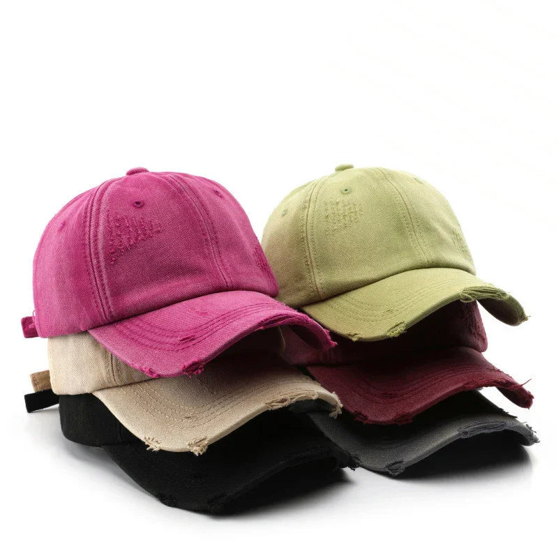 Stack of distressed cotton baseball caps in pink, green, beige, burgundy, black, and gray on white background