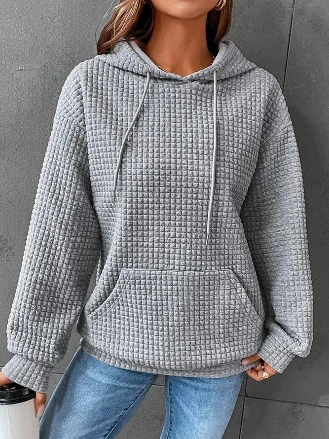 Woman wearing light grey textured waffle knit hoodie with front pocket and drawstrings, paired with blue jeans