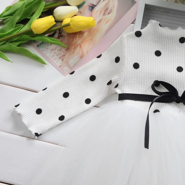 White ribbed long sleeve dress with black polka dots and black ribbon bow, yellow and white tulips nearby