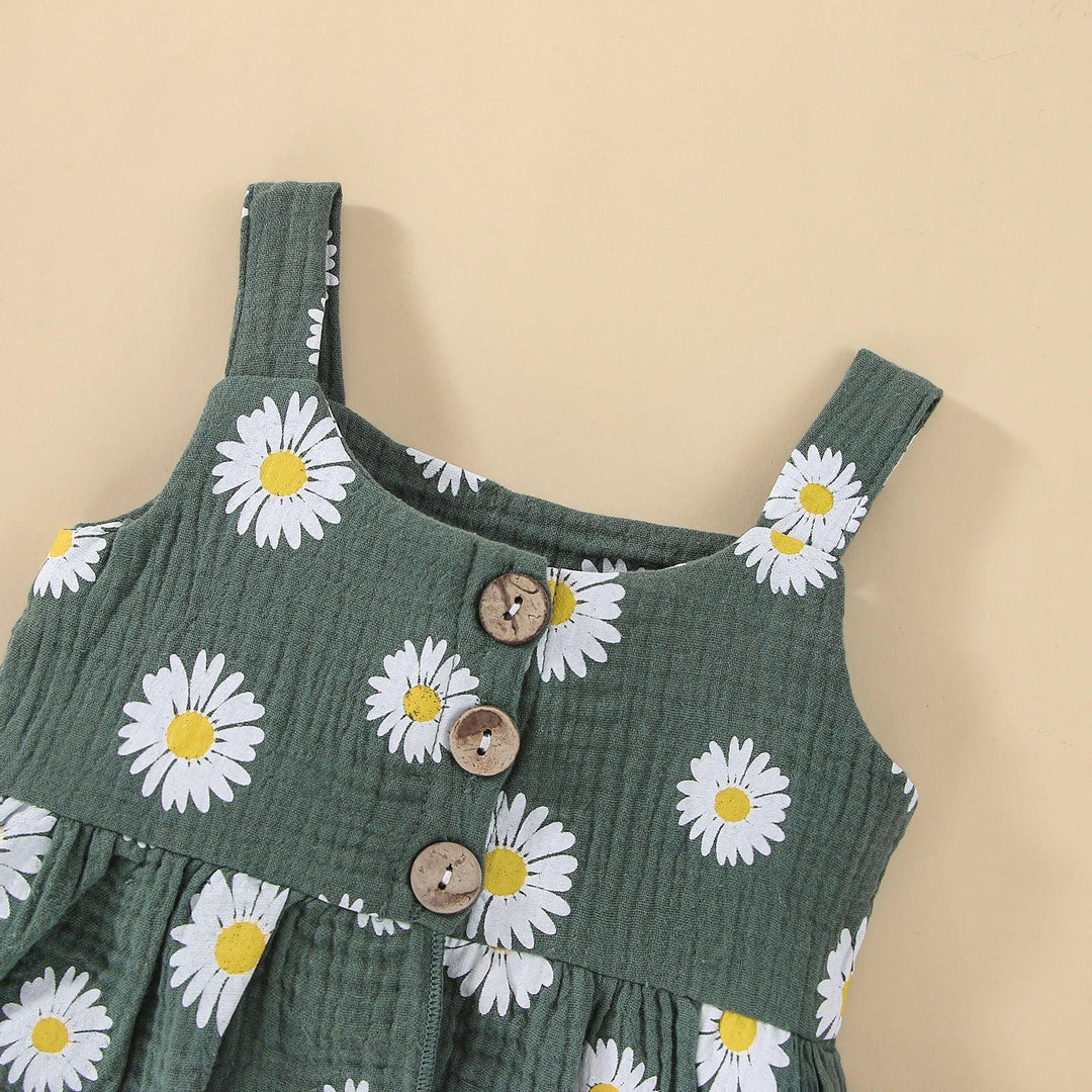 Green baby dress with white and yellow daisy print and brown wooden buttons on beige background